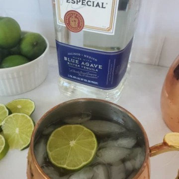 Mexican Mule text over a bottle of Jose Cuervo tequila and a copper mule mug and limes