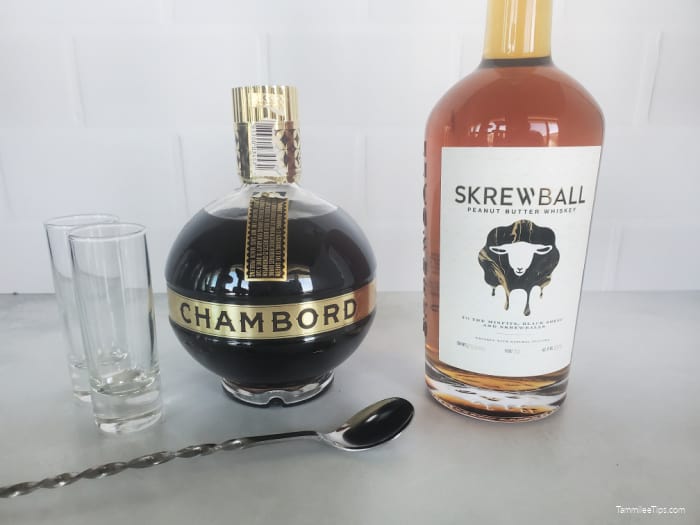 two empty shot glasses, a bartending spoon, bottle of Chambord, and Bottle of Skrewball peanut butter Whiskey
