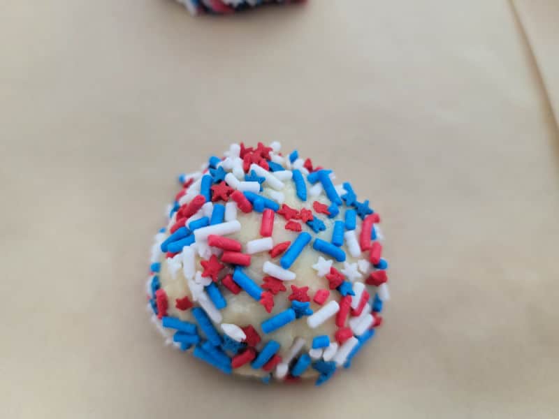 Cookie dough ball covered in red white and blue sprinkles sitting on parchment paper 
