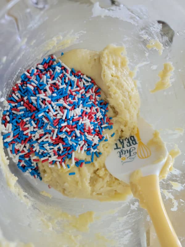 red white and blue sprinkles on top of cookie dough in a glass bowl with a spatula