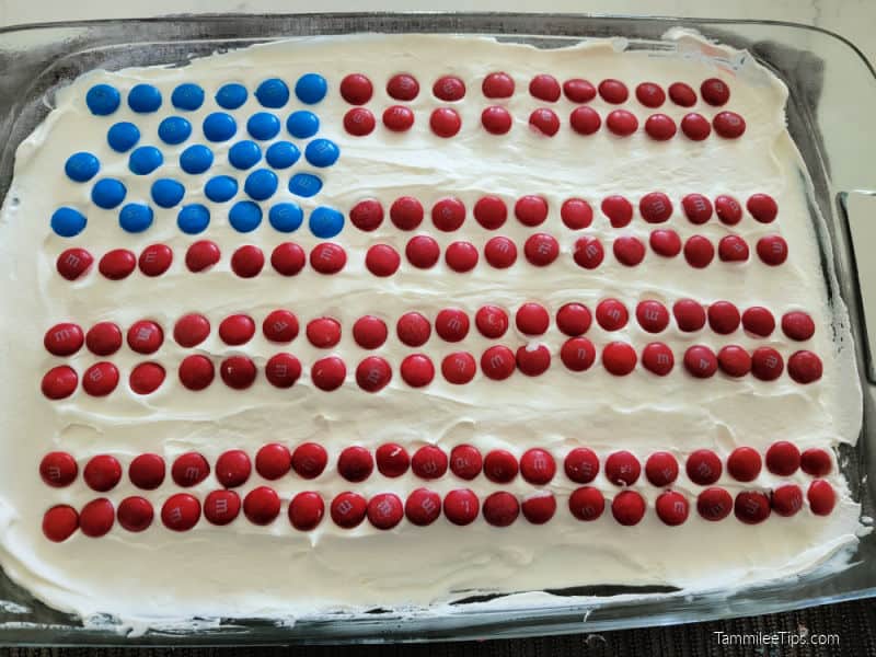 M&M American Flag on top of a red white and blue poke cake in a glass cake pan