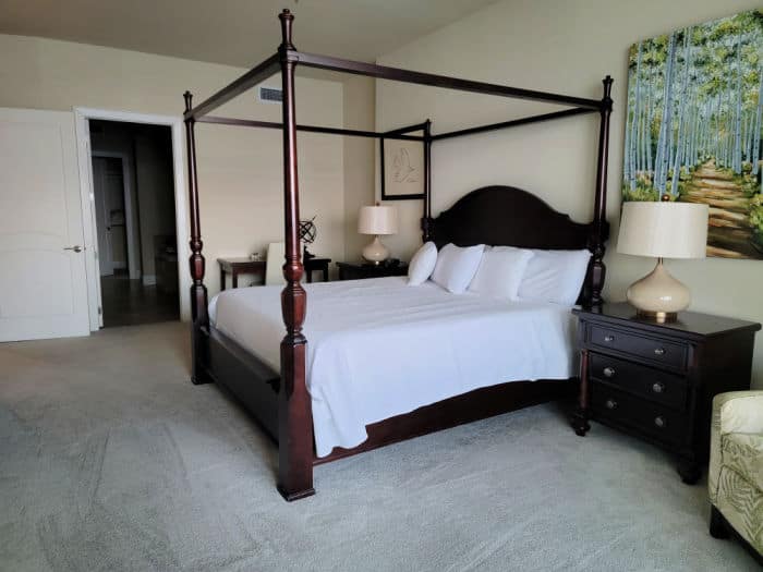 four poster bed with white linens, nightstand and chair