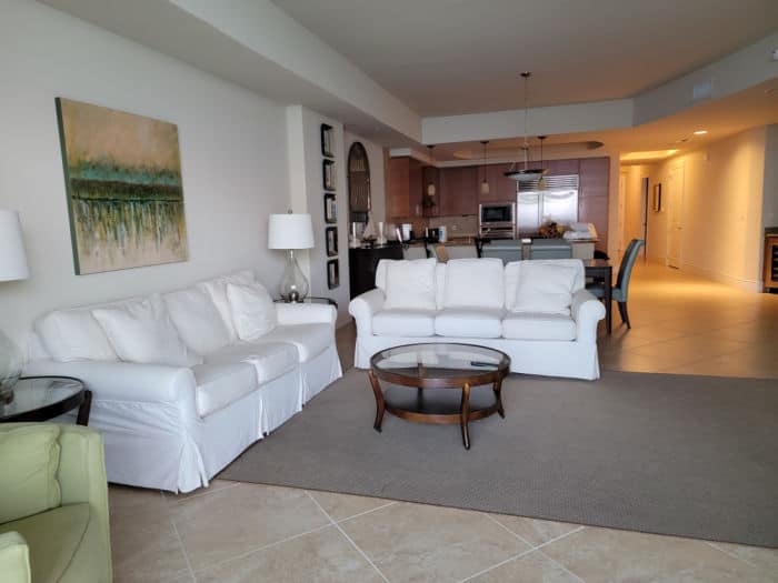 White couches and loveseat, table, and kitchen