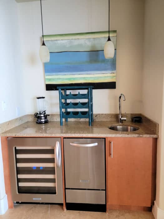 art hanging above a small counter area with wine fridge, ice maker, and sink