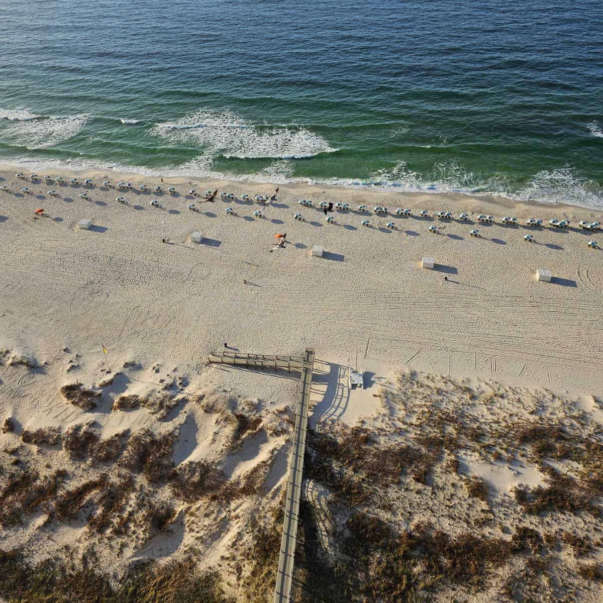 wooden boardwalk leading over sand dunes to white sand beaches with chairs and umbrellas and the coast of the Gulf of Mexico