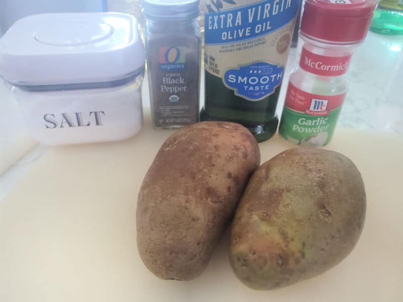 Russet potatoes, salt, pepper, olive oil, and garlic powder on a cutting board