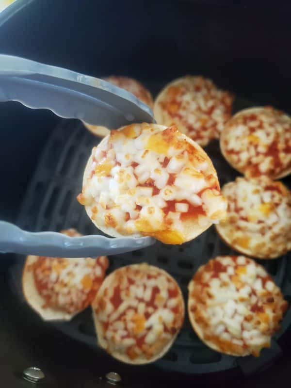 kitchen tongs holding a pizza bagel bite over the air fryer basket