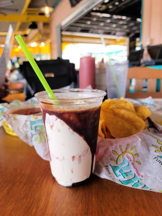 Bushwacker in a plastic cup with neon green straw next to a platter of Lulu's chips and salsa