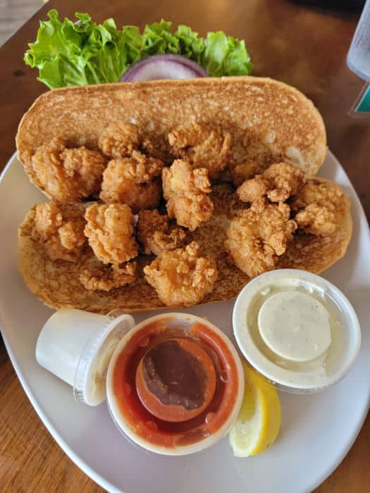 Shrimp po boy on a white plate with condiments, lettuce, and red onion