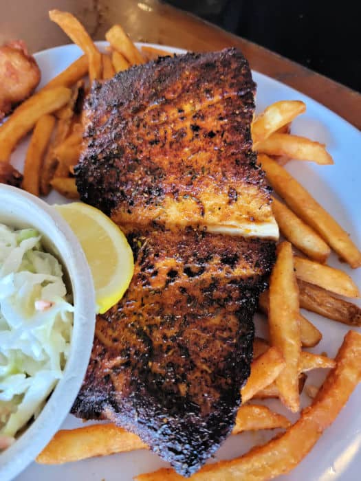 Blackened fish on a bed of French Fries next to Coleslaw 