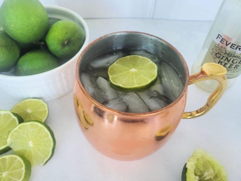 Mexican mule cocktail in a copper mule mug with lime slices and a bottle of ginger beer