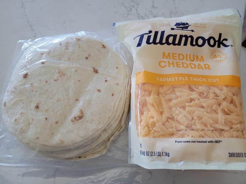 stack of tortillas and a bag or Tillamook medium cheddar cheese on a white counter. 