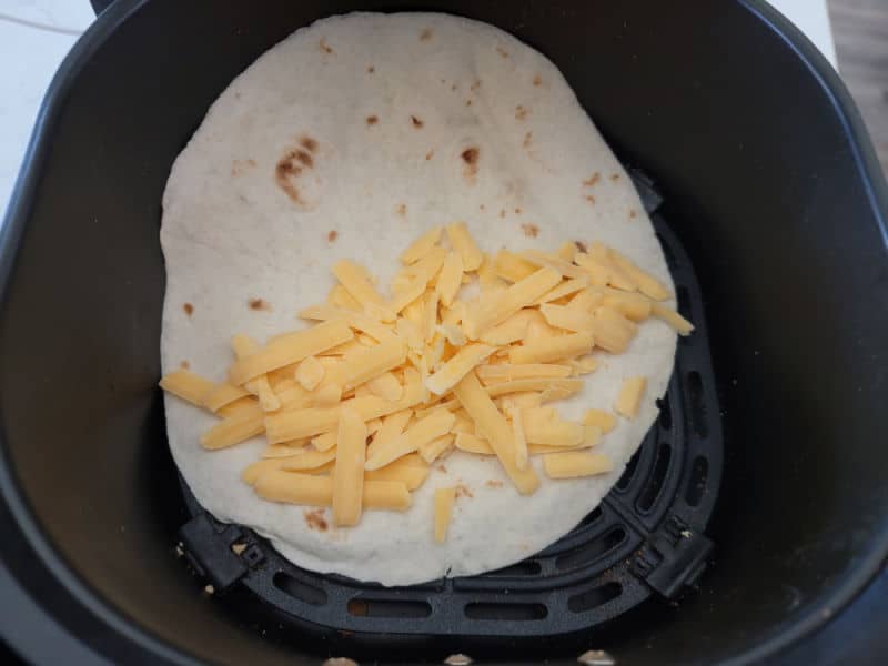 shredded cheese on a tortilla in the air fryer basket