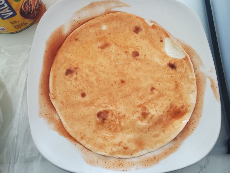 Tortilla soaking in enchilada sauce on a white plate