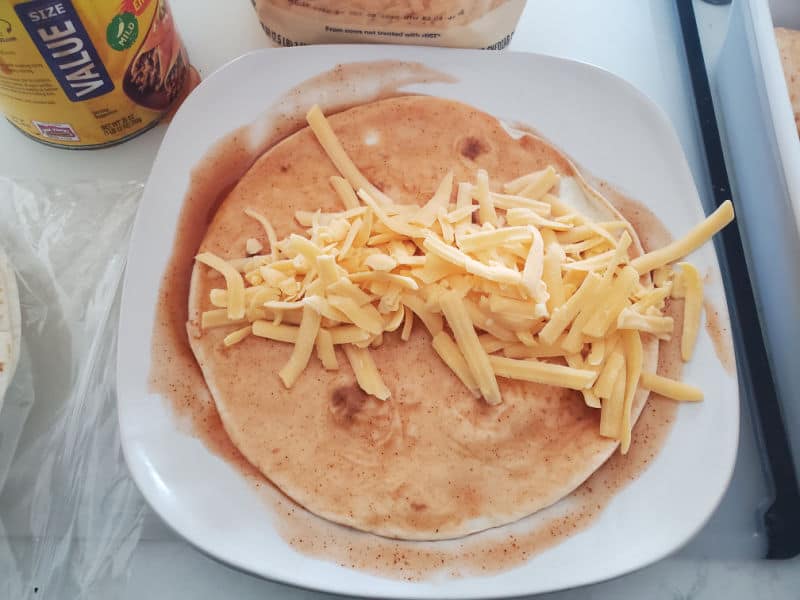 tortilla with enchilada sauce with a strip of shredded cheese down the middle on a white plate