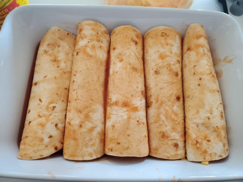 rolled tortillas in enchilada sauce in a white baking dish