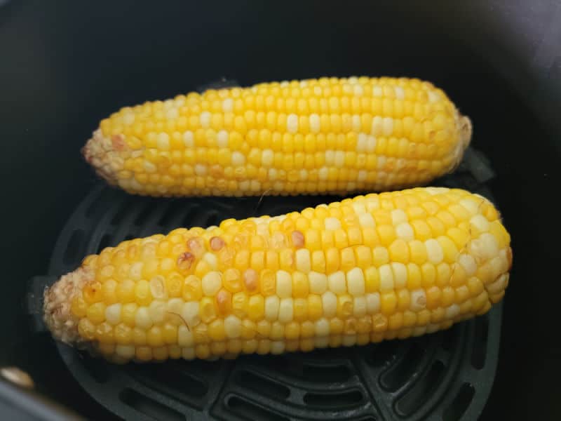 Two corn on the cob pieces sitting in an air fryer basket