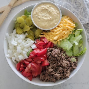 big mac salad in a white bowl with onions, tomatoes, ground beef, pickles, shredded cheese, lettuce, pickles, and big mac sauce