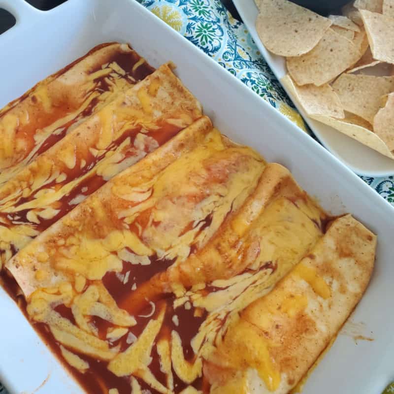 cheese enchiladas in a white casserole dish next to a bowl of tortilla chips
