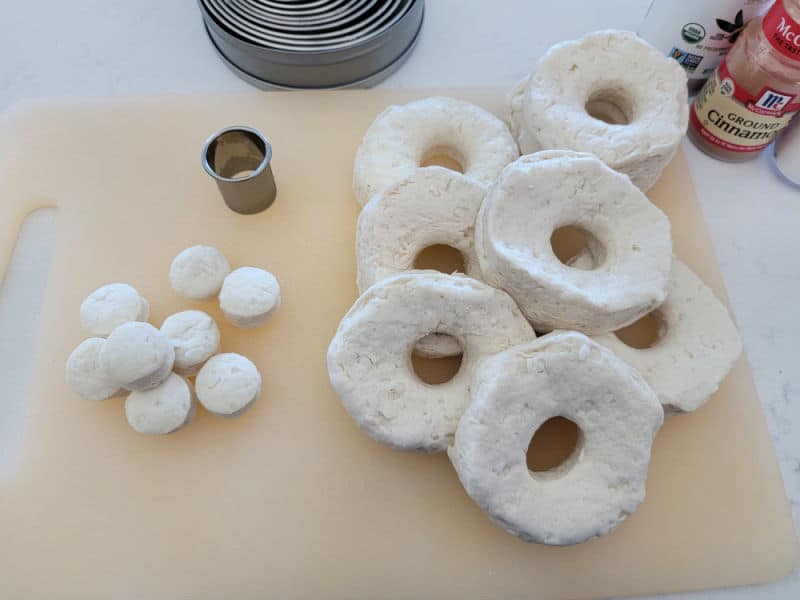 Air fryer donuts with a biscuit cutter on a cutting board before air frying. 