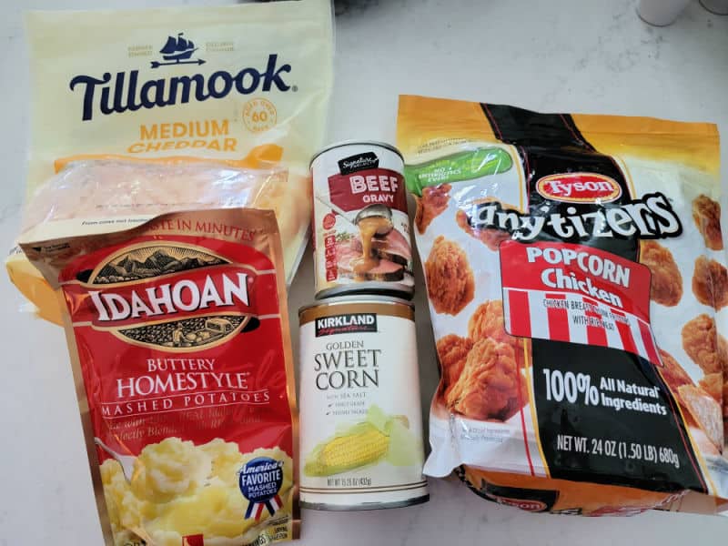 Tillamook cheddar cheese, Idahoan Mashed potatoes, corn, beef gravy, and Tyson popcorn chicken on a white counter 
