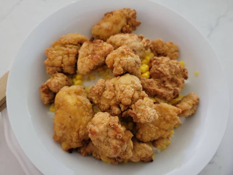 Popcorn chicken on top of corn and mashed potatoes in a white bowl 