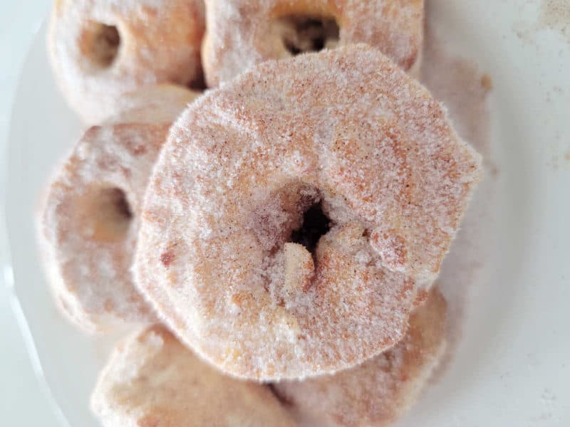 Air Fryer Donuts piled on a white plate with cinnamon sugar. 