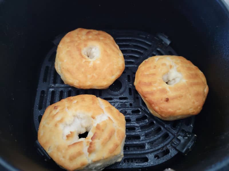 Three air fryer donuts on a greased air fryer basket. 