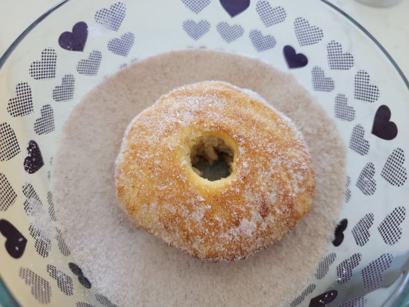 Air fryer donut in a bowl of cinnamon sugar. 