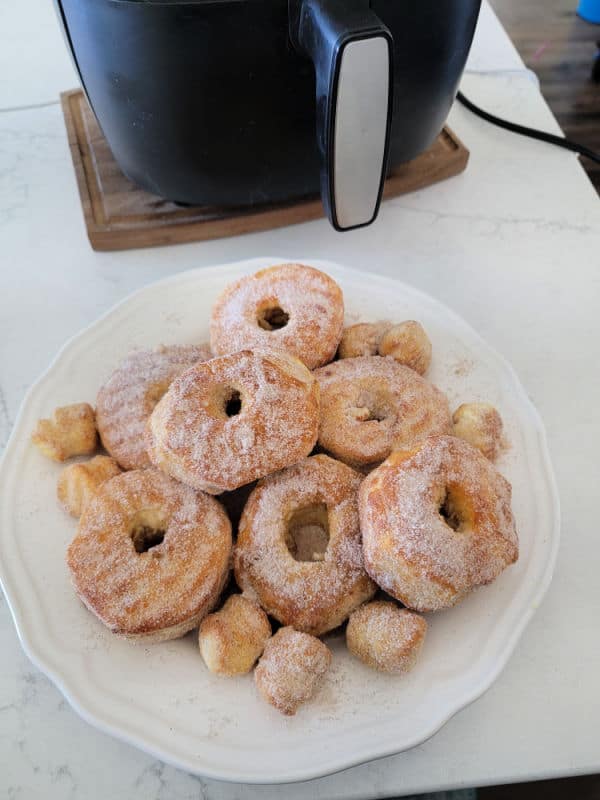 White plate filled with air fryer doughnuts with air fryer in the background. 