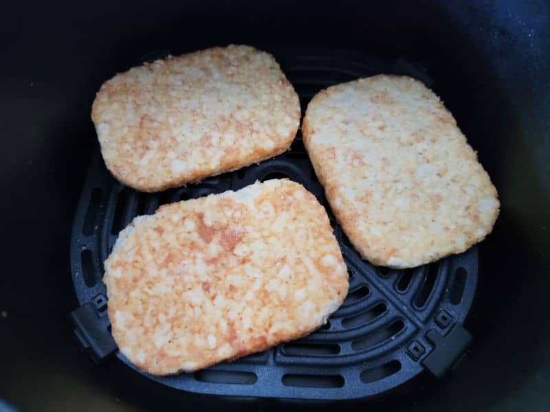 Frozen hashbrown patties in an air fryer basket