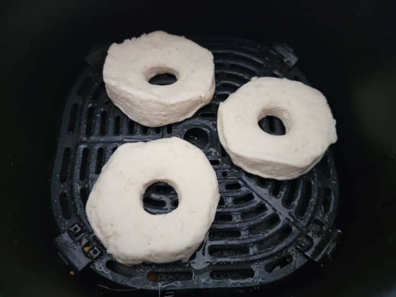 three Air fryer biscuit donuts on a greased air fryer basket for air frying