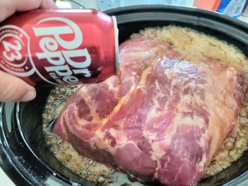 Dr pepper can pouring over a pork but in a slow cooker bowl 