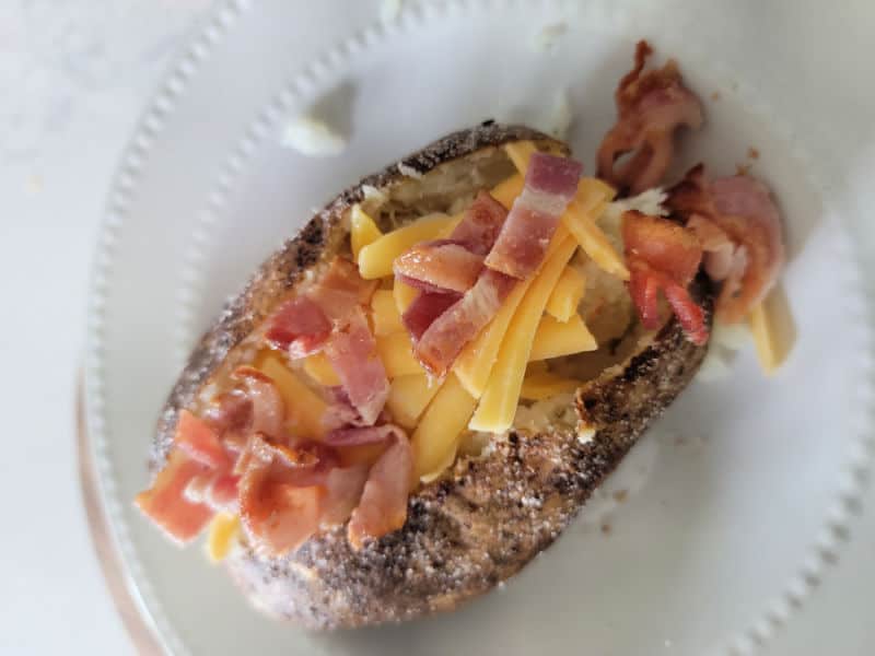 air fryer baked potato on a white plate garnished with bacon and cheese