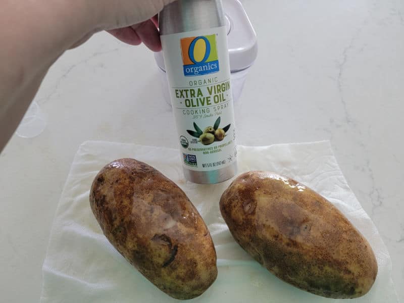 olive oil spray held next to two potato on a napkin