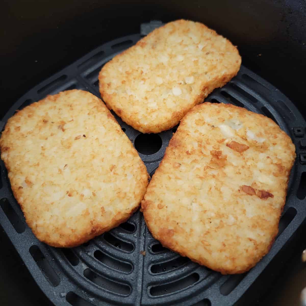 three frozen hashbrown patties in an air fryer basket