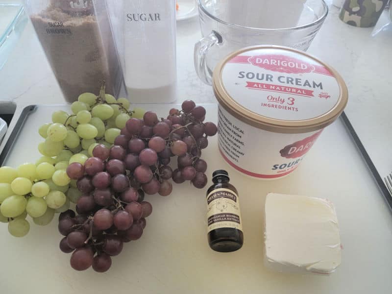 brown sugar, granulated sugar, glass bowl, sour cream, red and green grapes, vanilla, and cream cheese on a counter