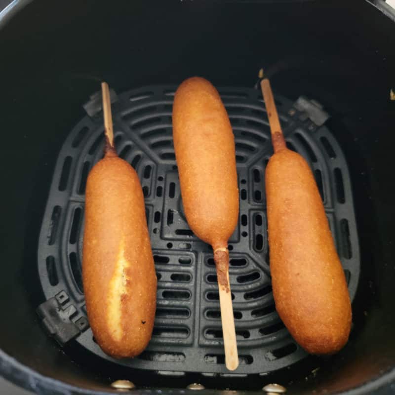 Three air fried corndogs in an air fryer basket