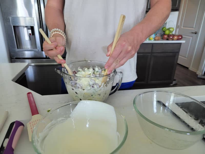 Hands mixing salad in a glass bowl with two wooden spoons