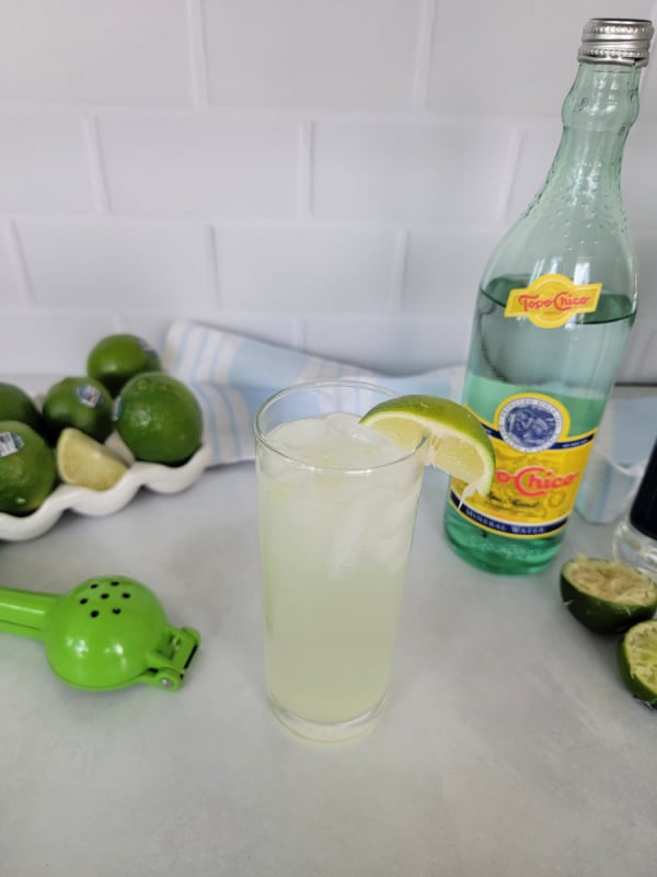 Ranch Water cocktail in a tall glass with al lime wedge, Topo Chico , limes, and lime squeezer