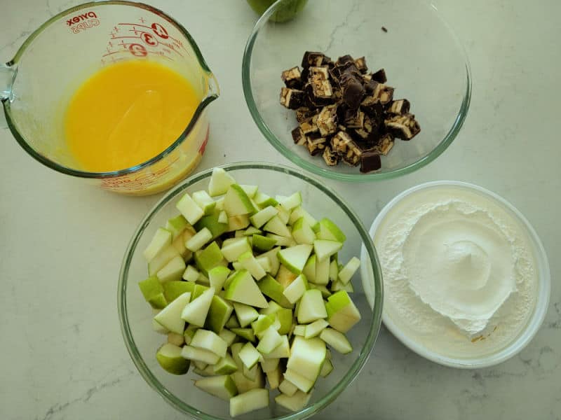pudding, cut up snickers bars, diced apples, and cool whip open container on a white countertop for snickers apple salad. 