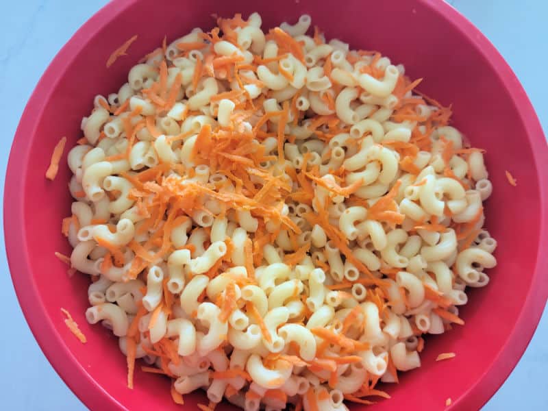 Cooked macaroni pasta and shredded carrots in a large red bowl