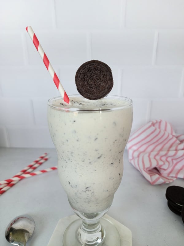 Oreo Milkshake in a tall glass with red striped straw and Oreo Garnish