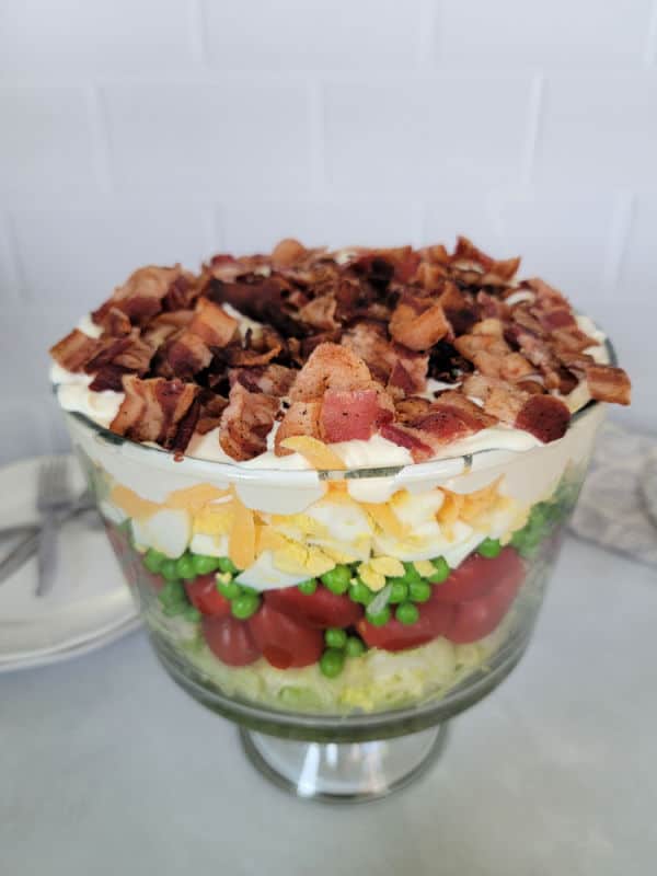 7 layer salad in a trifle bowl with bacon on top, on a white counter. 