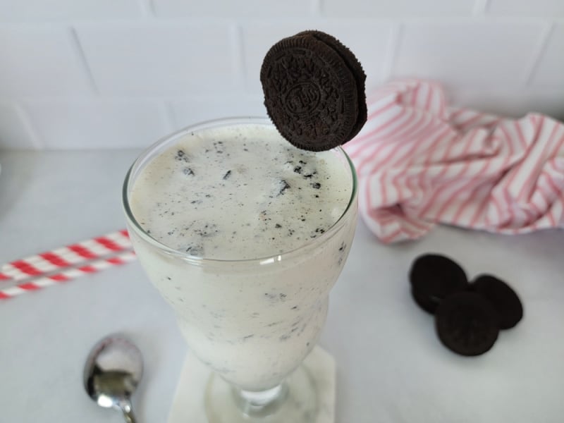 Oreo Shake with an Oreo garnish in a glass mug next to a spoon and additional Oreos