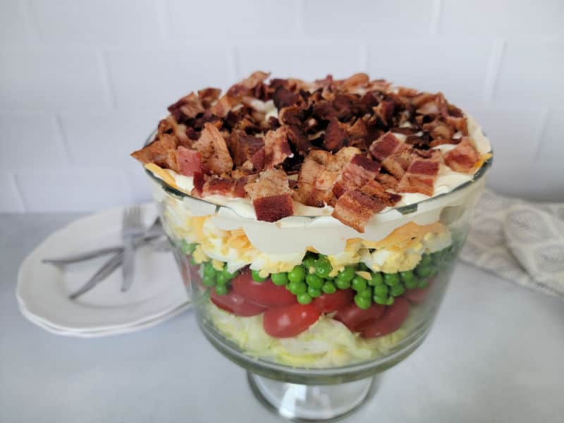 Classic 7 layer salad in a trifle dish with small plates and forks behind it. 