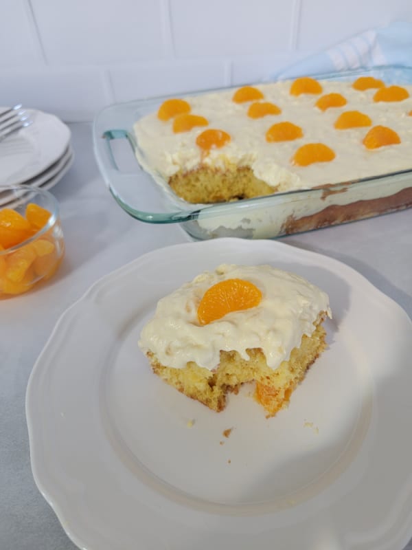 square of cake on a white plate next to a baking dish of pig pickin cake