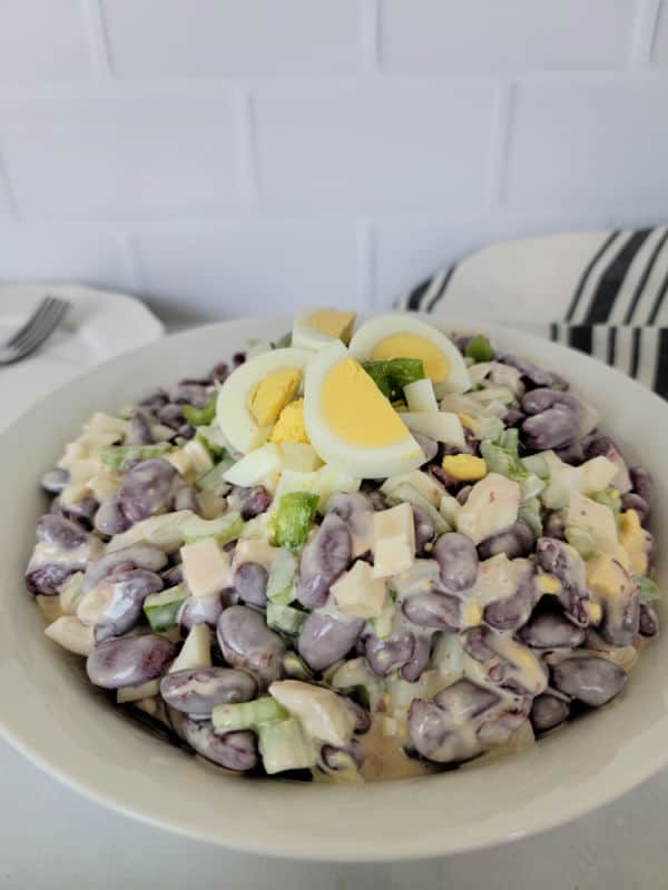 Hard boiled eggs cut into slices on kidney bean salad in a white bowl next to a cloth napkin