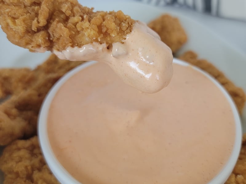 Chicken finger coated in pink mayo over a white bowl and other chicken fingers. 