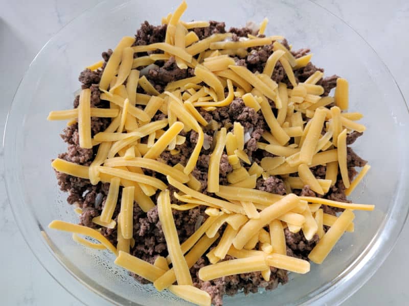 Shredded cheddar cheese on ground beef for Impossible Cheeseburger Pie Bisquick